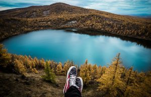 Person's feet submerged in the calm waters of a jungle lake, surrounded by lush greenery.