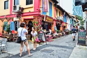 A woman strolls along a narrow street lined with vibrant, colorful buildings, creating a lively urban atmosphere.