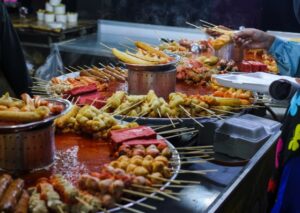  A man skillfully prepares skewered food at a bustling food stand, showcasing his culinary expertise and vibrant atmosphere.