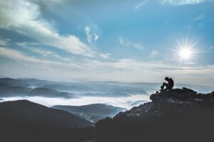  A person sits atop a mountain, basking in the warm sunlight, surrounded by a breathtaking landscape.