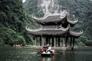 A couple enjoys a serene moment in a boat on the water, with a picturesque pagoda in the background.