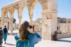 A woman captures a photograph of the historic skyline of the old city of Jerusalem, showcasing its ancient architecture.