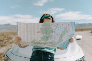 A girl stands in front of her car, holding a map and looking thoughtfully into the distance.