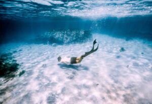 A man swims gracefully underwater in the ocean, showcasing the beauty of marine life in an ecotourism setting.