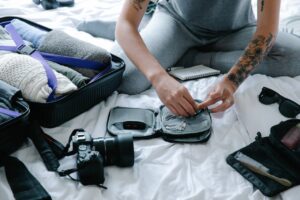 A woman with tattoos sits on a bed, surrounded by her luggage, exuding a sense of adventure and personal style.