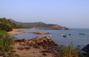 A serene beach scene featuring boats anchored near the shore, surrounded by lush trees and gentle waves.