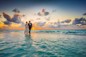  A wedding couple embraces on the beach, silhouetted against a vibrant sunset, capturing a moment of love and joy.