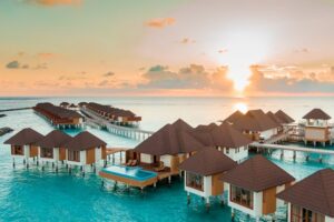 A stunning view of a luxury resort in the Maldives, featuring overwater bungalows and crystal-clear turquoise waters.