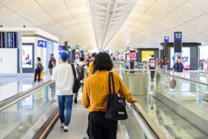 A group of travelers descends an escalator in a bustling airport terminal, showcasing the movement of airport traffic.